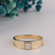 a yellow gold ring with a single diamond in the center on a white table next to blue flowers