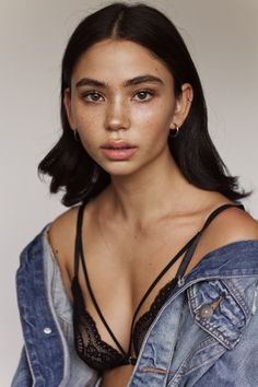 a woman with freckled hair wearing a denim shirt and earrings is looking at the camera