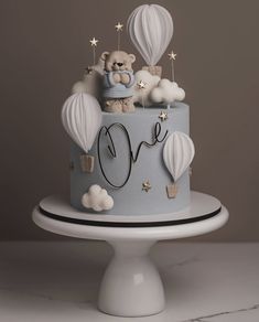 a blue cake decorated with hot air balloons and a teddy bear on top that says love