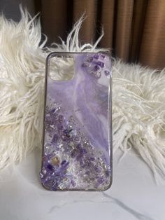 an iphone case with purple and silver glitters on it sitting on a white furnishing