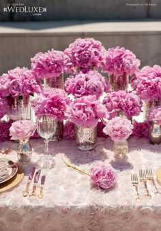 a table topped with lots of pink flowers next to silverware and forks on top of a white table cloth