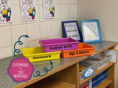 some bins that are sitting on top of a desk in a classroom with posters