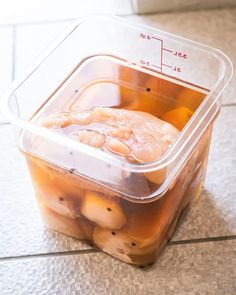 a plastic container filled with food sitting on top of a tiled floor next to a measuring cup