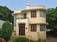 a house with red trim on the front and side windows, surrounded by greenery