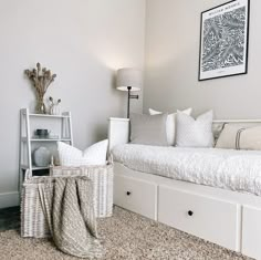 a white day bed sitting in a bedroom next to a shelf with pillows on it