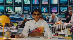 a man wearing sunglasses sitting at a table in front of televisions and other objects