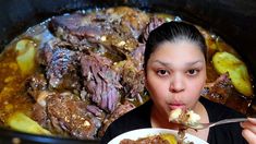 a woman eating food out of a bowl in front of a pot full of meat and potatoes