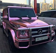 a pink mercedes g - class is parked on the side of the road in front of other cars