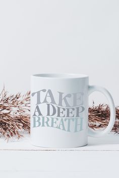 a white coffee mug with the words take a deep breath on it next to dried grass