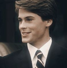 a young man in a suit and tie smiles at the camera while looking to his left