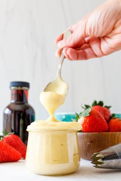 a person holding a spoon full of mayonnaise with strawberries in the background