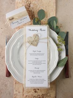 a table setting with place cards, silverware and greenery on the plate holders