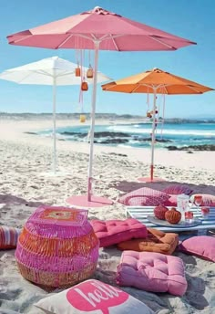 pink and yellow umbrellas on the beach with pillows, blankets and cushions in the sand