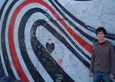 a young man standing in front of a wall with graffiti on it and writing all over it