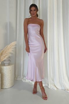 a woman standing in front of a white curtain wearing a pink strapless dress and sandals