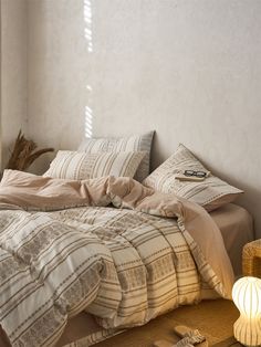 an unmade bed in a bedroom with white walls and wooden flooring next to a window