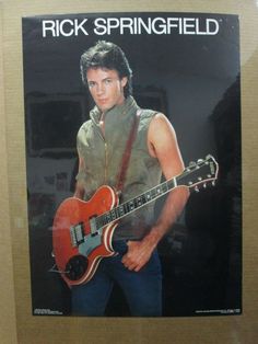 a man holding a red guitar in his right hand and wearing a brown shirt with the words rick springfield on it