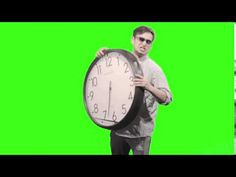 a man holding a large clock while standing in front of a green screen