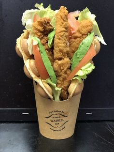 a cup filled with chicken and lettuce wrapped in bread on top of a table