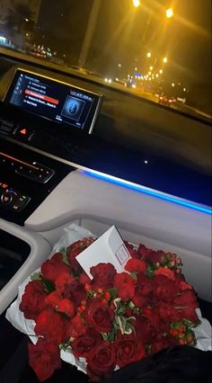 a bunch of red roses sitting on the dashboard of a car with an electronic screen in the background