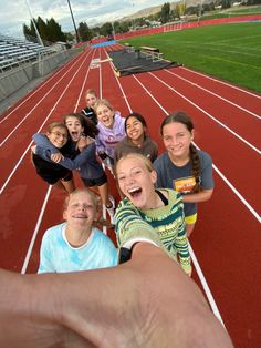 a group of kids taking a selfie on a running track with their hands in the air