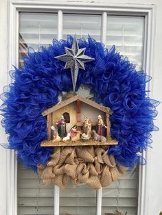 a nativity scene is hanging on the front door with burlap and blue wreath