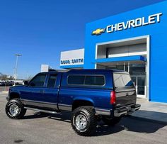 a blue pick up truck parked in front of a chevrolet dealership