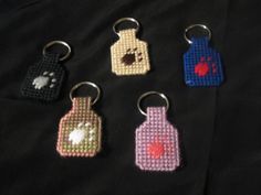 four different colored bottle shaped keychains on a black cloth covered table with red and white paw prints