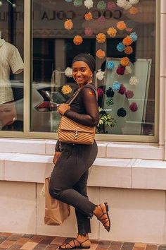 a woman standing in front of a store window holding a brown bag and smiling at the camera