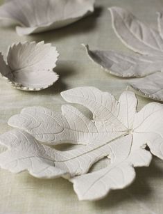 three white leaf shaped dishes sitting on top of a cloth covered tablecloth with two leaves in the middle