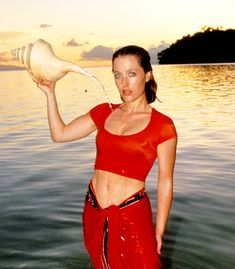 a woman is standing in the water with a jug on her head and wearing red pants