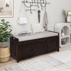 a living room with white walls and wooden flooring, a brown storage bench next to a potted plant