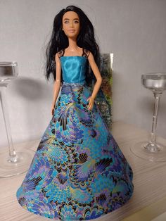 a barbie doll wearing a blue dress and holding a wine glass on a wooden table