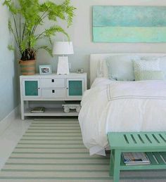 a white bed sitting next to a green plant on top of a wooden table in a bedroom