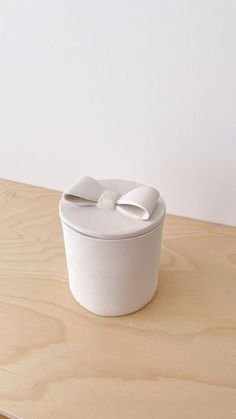 a white ceramic container with a bow on the lid sitting on a wooden table next to a wall