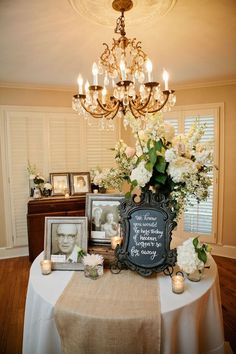 a table with flowers, candles and pictures on it in front of a chandelier