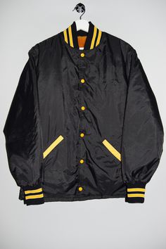 "Vintage varsity jacket from the 80's, 90's in black with yellow stipes and buttons and soft lining. - Fabric: Shell: 100% Nylon Lining: 100% Cotton - Size tag: Please always check measurements before buying. Men's S. - Measurements (laying flat): Pit to Pit: 23\" Length: 28\" Sleeve: 25\" Pit to Cuff: 21\" Across the shoulders: 19\" -Wear: /Please see images for details/ Very good used condition and a great vintage find. -Flaws: / serious wear, tears, holes, marks or stains/ None . *All of our items are preloved pieces so some signs of natural wear and age are to be expected. Please look through the photos carefully to check if the condition is to your satisfaction.  *All efforts are made to show any defects however small imperfections may be missed. In cases that we've missed a major fla Black Varsity Jacket For College With Button Closure, Black Varsity Jacket With Button Closure For College, Retro Black Varsity Jacket With Ribbed Cuffs, Vintage Black Varsity Jacket For Streetwear, Retro Black Varsity Jacket For College, Black School Varsity Jacket, Yellow Varsity Jacket For Streetwear, Yellow Varsity Outerwear For College, Retro Black Windbreaker For Fall