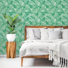 a bed sitting next to a green wallpaper covered in white pillows and blankets on top of a wooden headboard