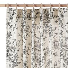 a curtain with floral print on it hanging from a wooden rod, in front of a white background