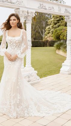 a woman in a wedding dress standing on a brick walkway with an archway behind her