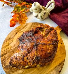 a piece of meat on a wooden cutting board next to a teapot and flowers