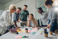 a group of people standing around a table with sticky notes on it and pencils in front of them