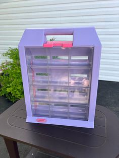 a purple plastic box sitting on top of a black table next to a green plant