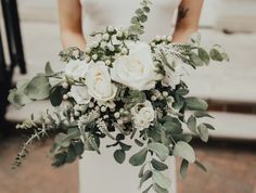 a bride holding a bouquet of white roses and greenery