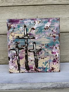 a painting with three crosses on it sitting on top of a wooden table next to a wall