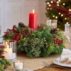 a christmas centerpiece with pine cones, berries and candles