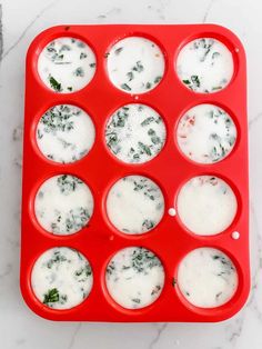 a red tray filled with cupcakes covered in white icing and spinach