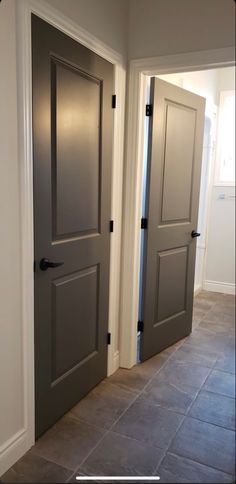 an empty hallway with two gray doors and tile flooring in front of the door