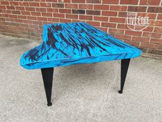 a blue and black coffee table sitting on top of a sidewalk next to a brick wall