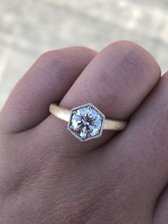 a person's hand holding a ring with a diamond in the middle and a white background